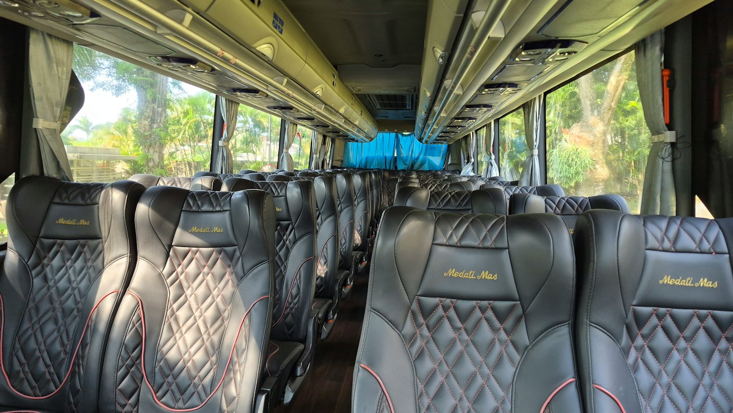 Rows of modern black leather bus seats with red stitching.