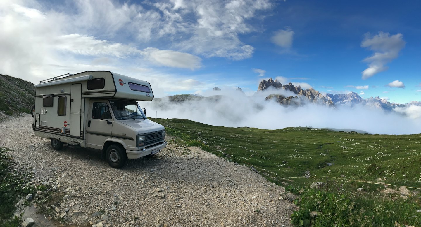 A campervan parked on a gravel road overlooking mountain peaks.